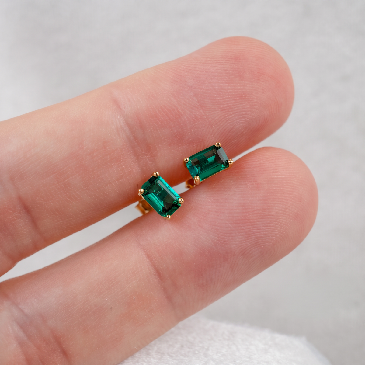 Lab emerald rectangle stud earrings in yellow gold-plated sterling silver shown on the hand