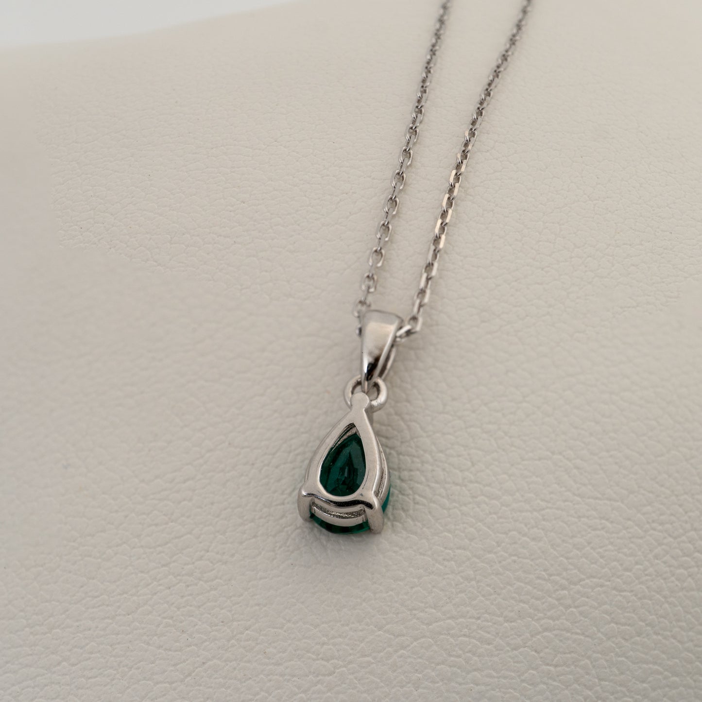 Silver necklace with a green teardrop pendant on a light gray background