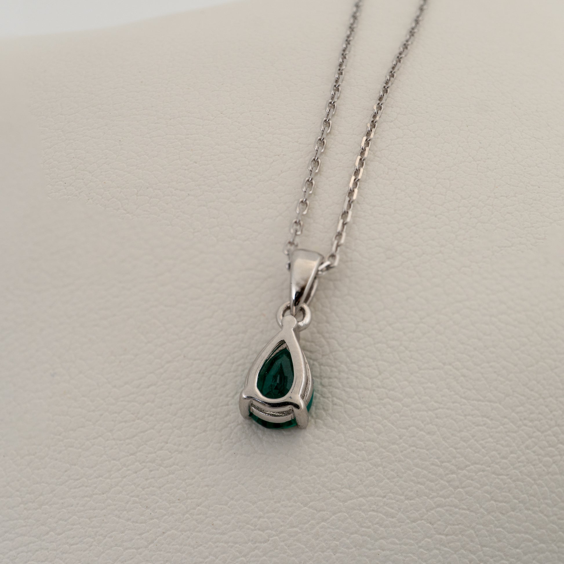 Silver necklace with a green teardrop pendant on a light gray background