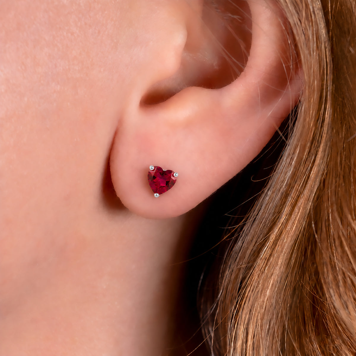 Lab grown ruby heart stud earring worn on the ear, showing its petite size