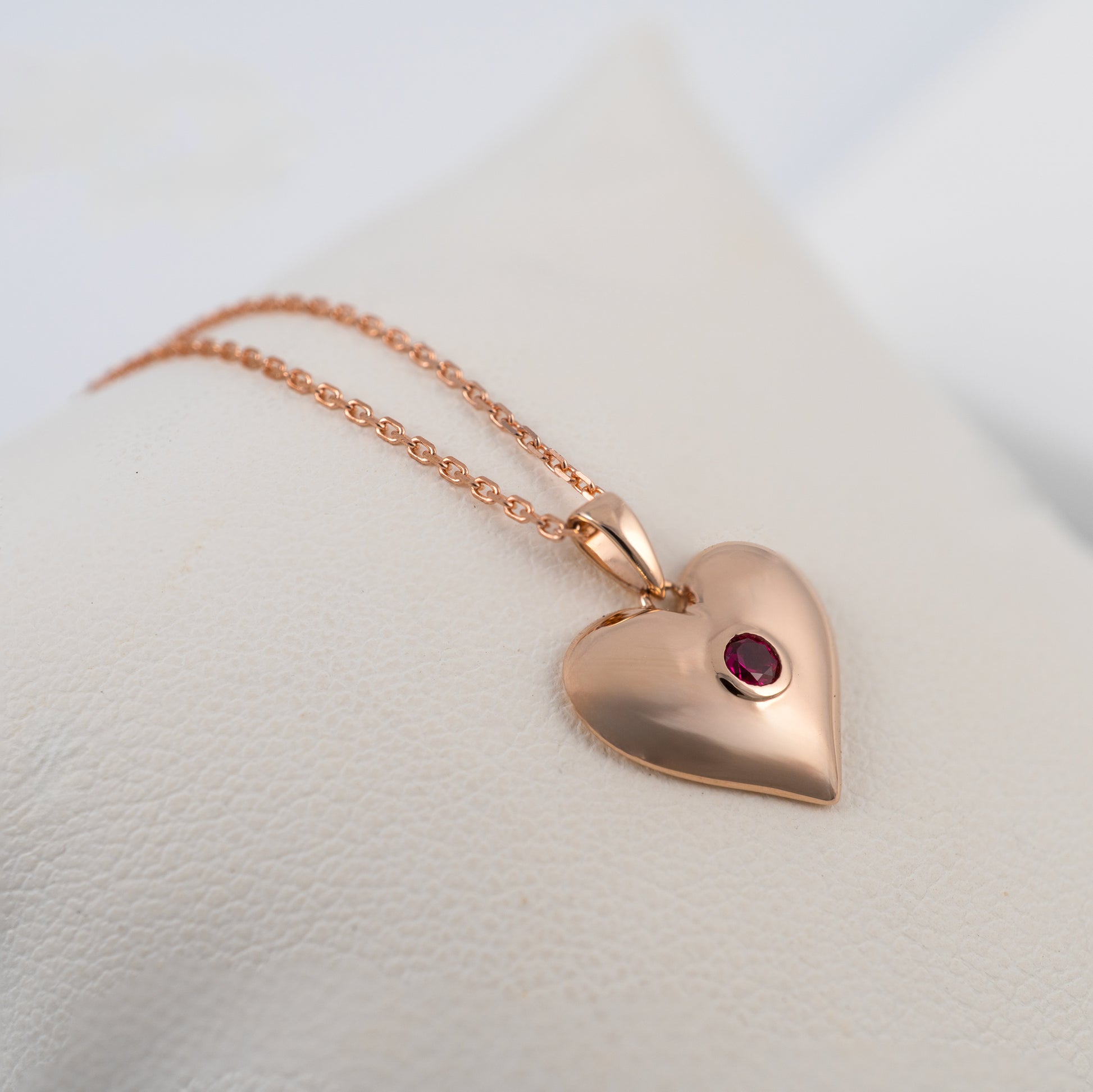 Side angle of rose gold heart necklace with lab-grown ruby highlighting curved, sculpted form