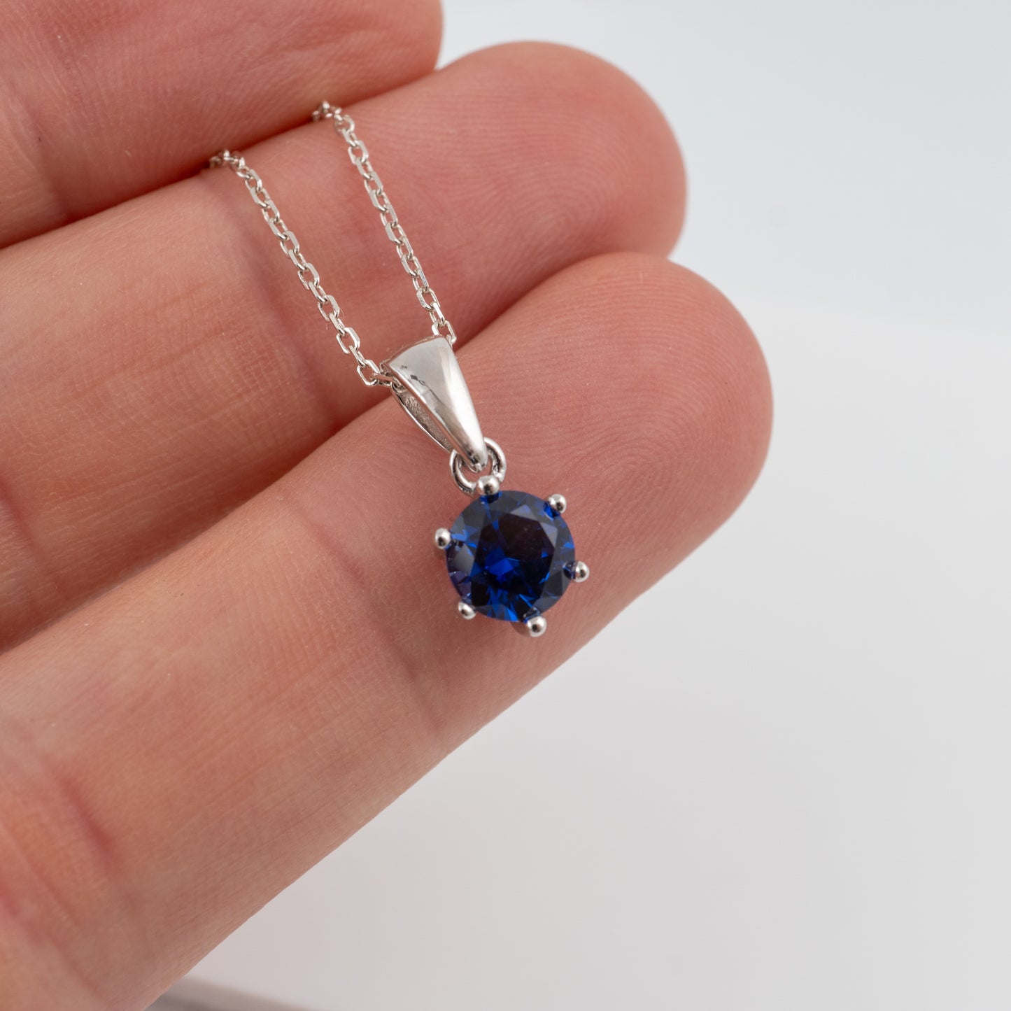 holding a silver lab grown sapphire necklacein hand to show the rich deep blue colour 