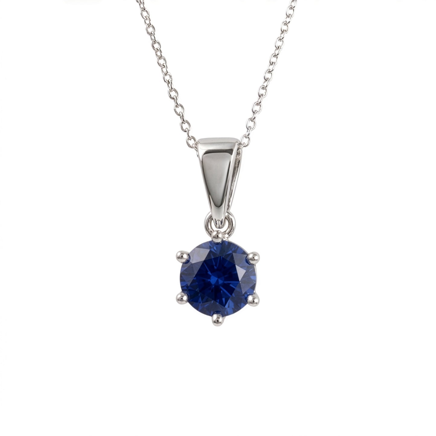 A silver and lab sapphire pendant necklace featuring a round-cut deep blue gemstone in a four-prong setting, suspended from a delicate silver chain against a plain white background.