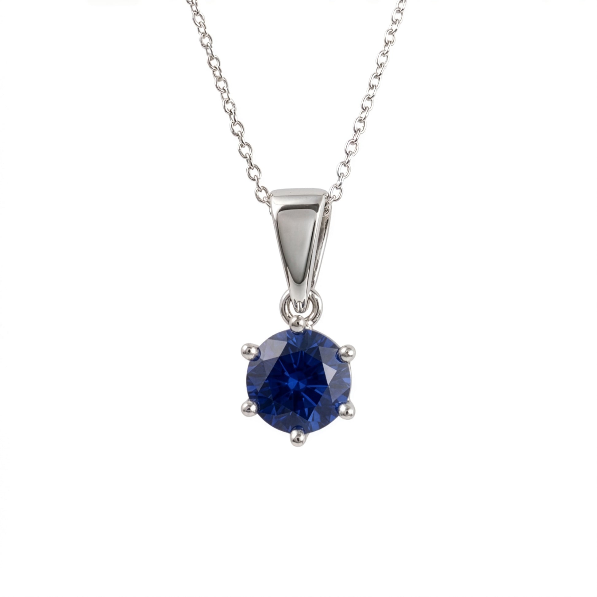 A silver and lab sapphire pendant necklace featuring a round-cut deep blue gemstone in a four-prong setting, suspended from a delicate silver chain against a plain white background.