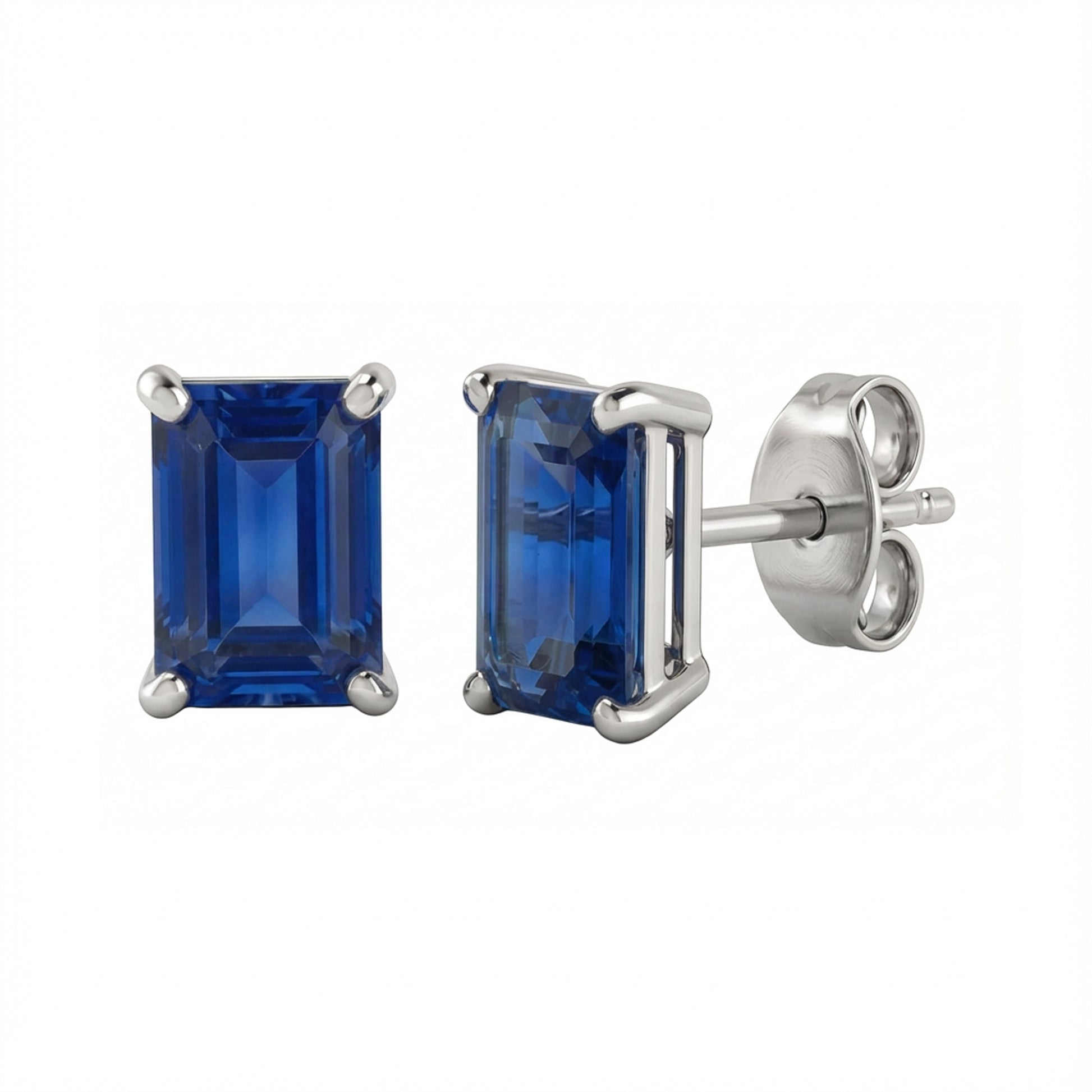 A pair of rectangular emerald-cut lab blue sapphire stud earrings in a silver-toned metal setting, with one earring facing forward and the other angled to show the post and butterfly back, on a plain white background.
