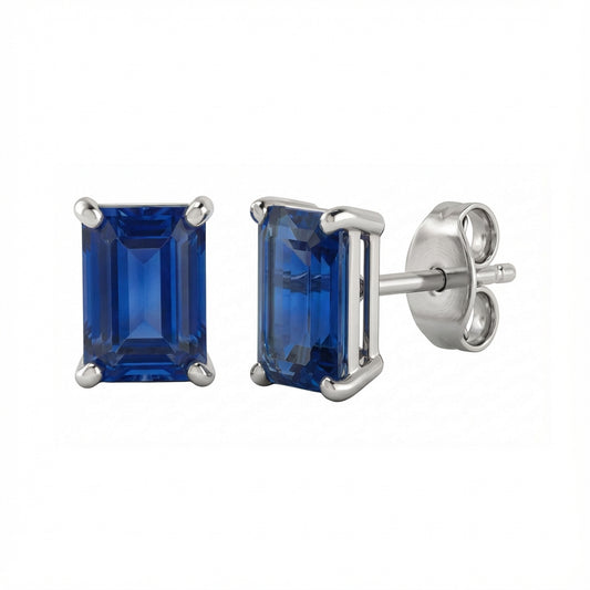 A pair of rectangular emerald-cut lab blue sapphire stud earrings in a silver-toned metal setting, with one earring facing forward and the other angled to show the post and butterfly back, on a plain white background.