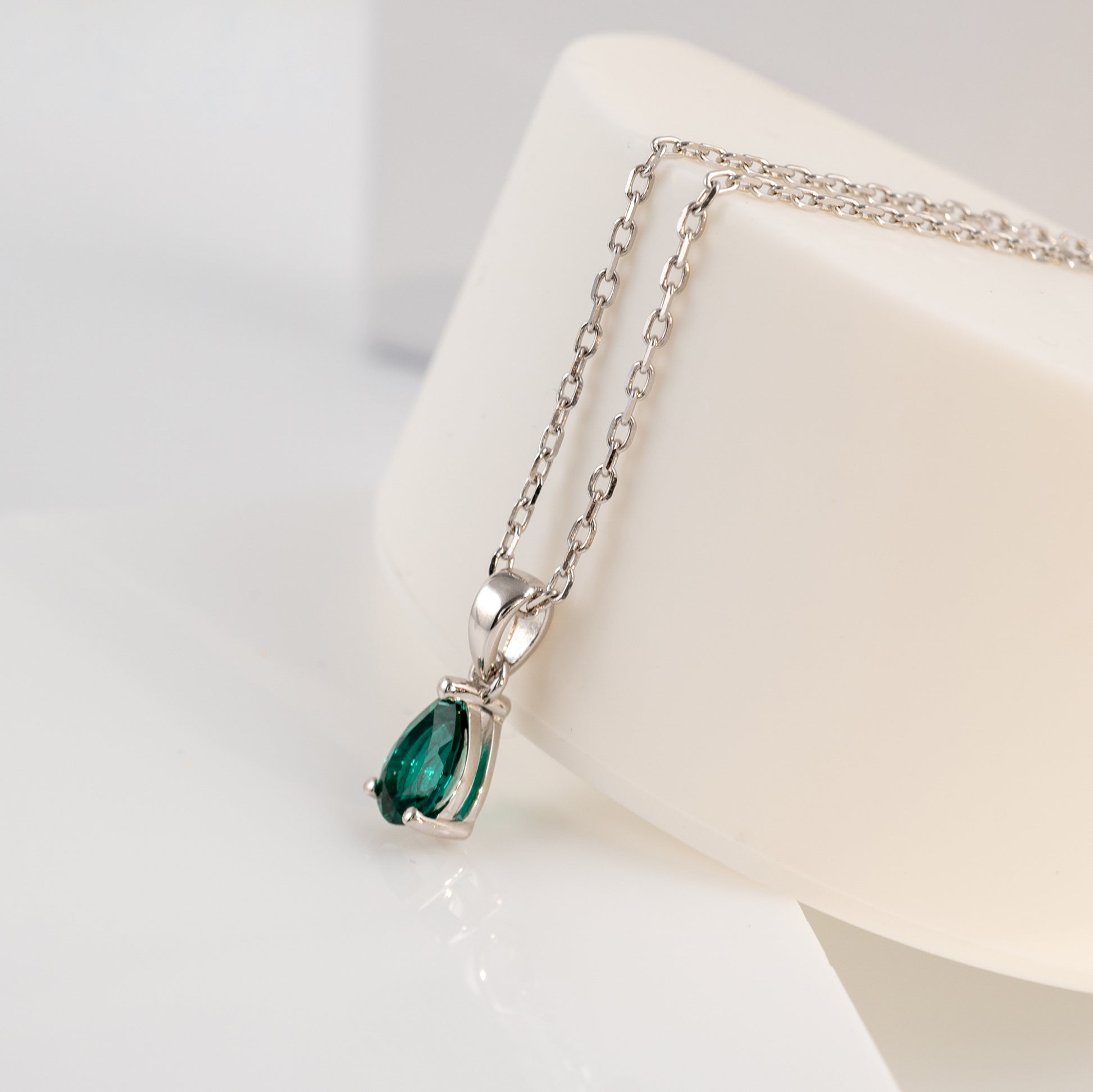 Silver necklace with a green teardrop pendant on a white stand.
