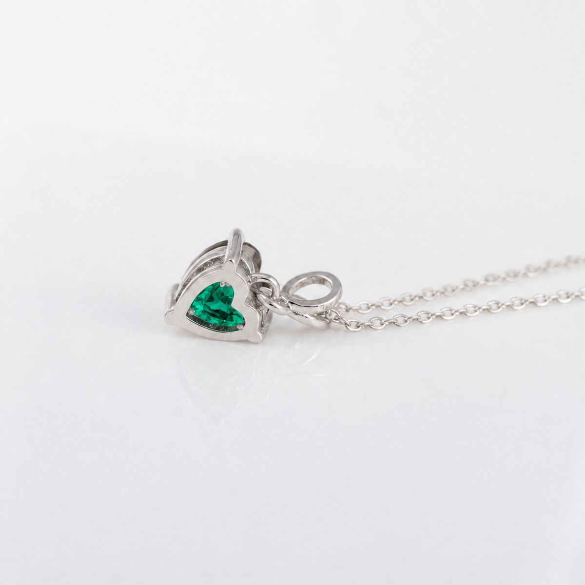 A silver heart-shaped pendant necklace featuring a vibrant green heart-shaped gemstone, displayed on a clean white background.