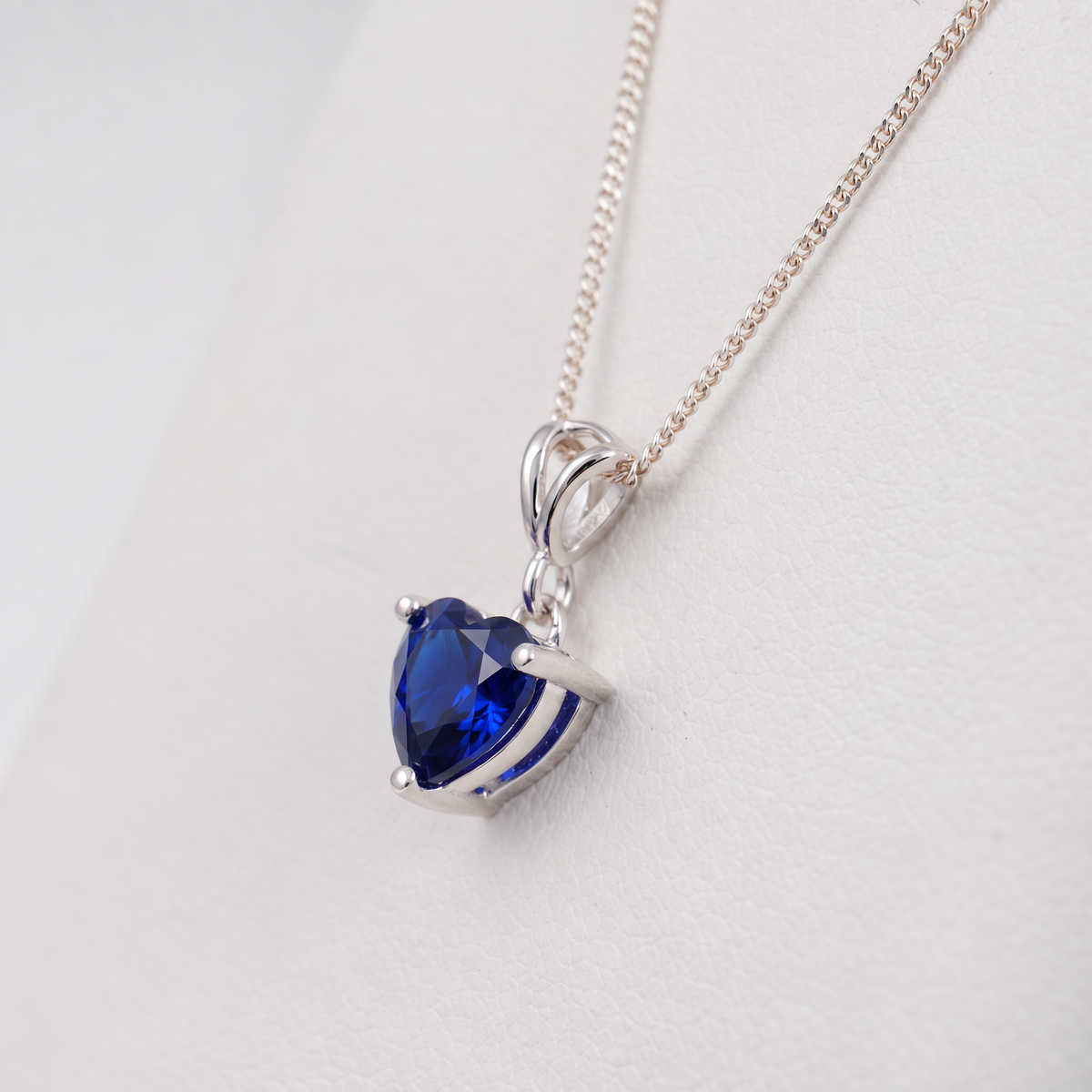lab blue sapphire heart necklace silver setting side angle view on a white display stand
