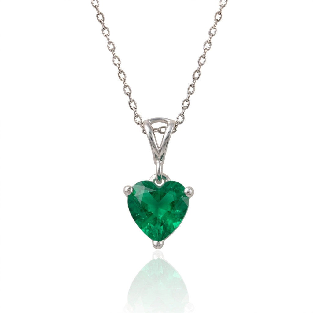 A heart-shaped lab emerald gemstone pendant necklace in a silver-toned setting on a delicate silver chain, shown against a white background with a soft reflection below.