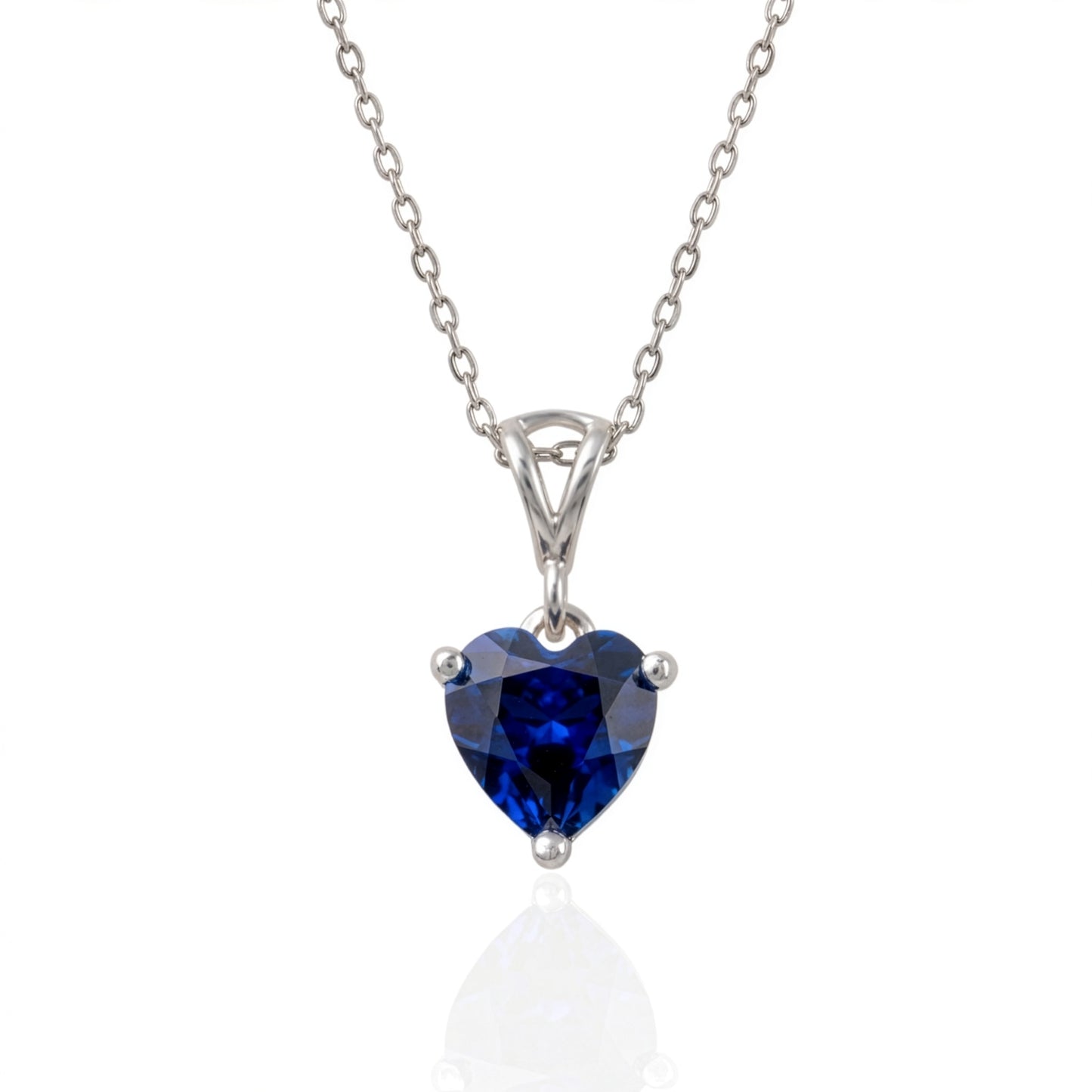 A heart-shaped lab sapphire gemstone pendant necklace in a silver-toned prong setting on a delicate silver chain, shown against a white background with a soft reflection below.