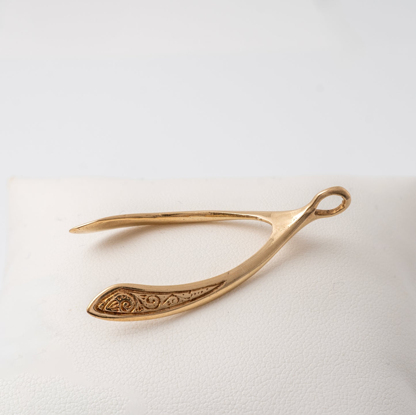 Detailed close-up of a vintage large gold wishbone pendant, highlighting its scrollwork design on the sides