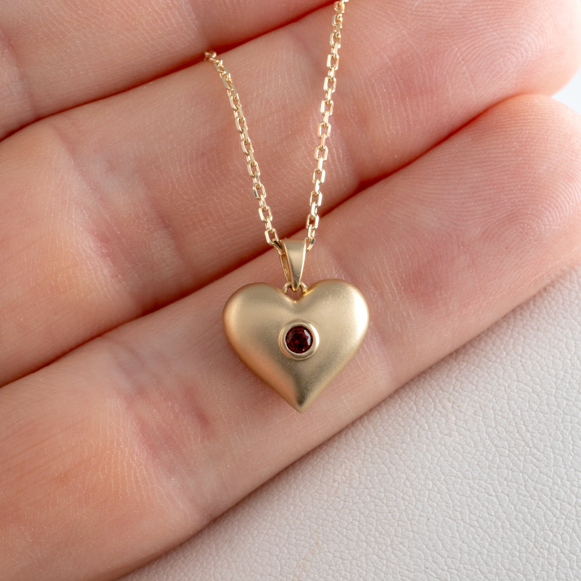 Heart-shaped pendant in matte gold with garnet stone in a hand