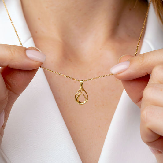 Gold necklace with a teardrop pendant held by hands against a white background