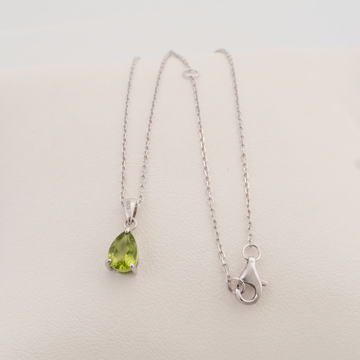 Natural peridot teardrop necklace laid on a white cushion, showing the sterling silver cable chain, lobster clasp and adjustment rings.