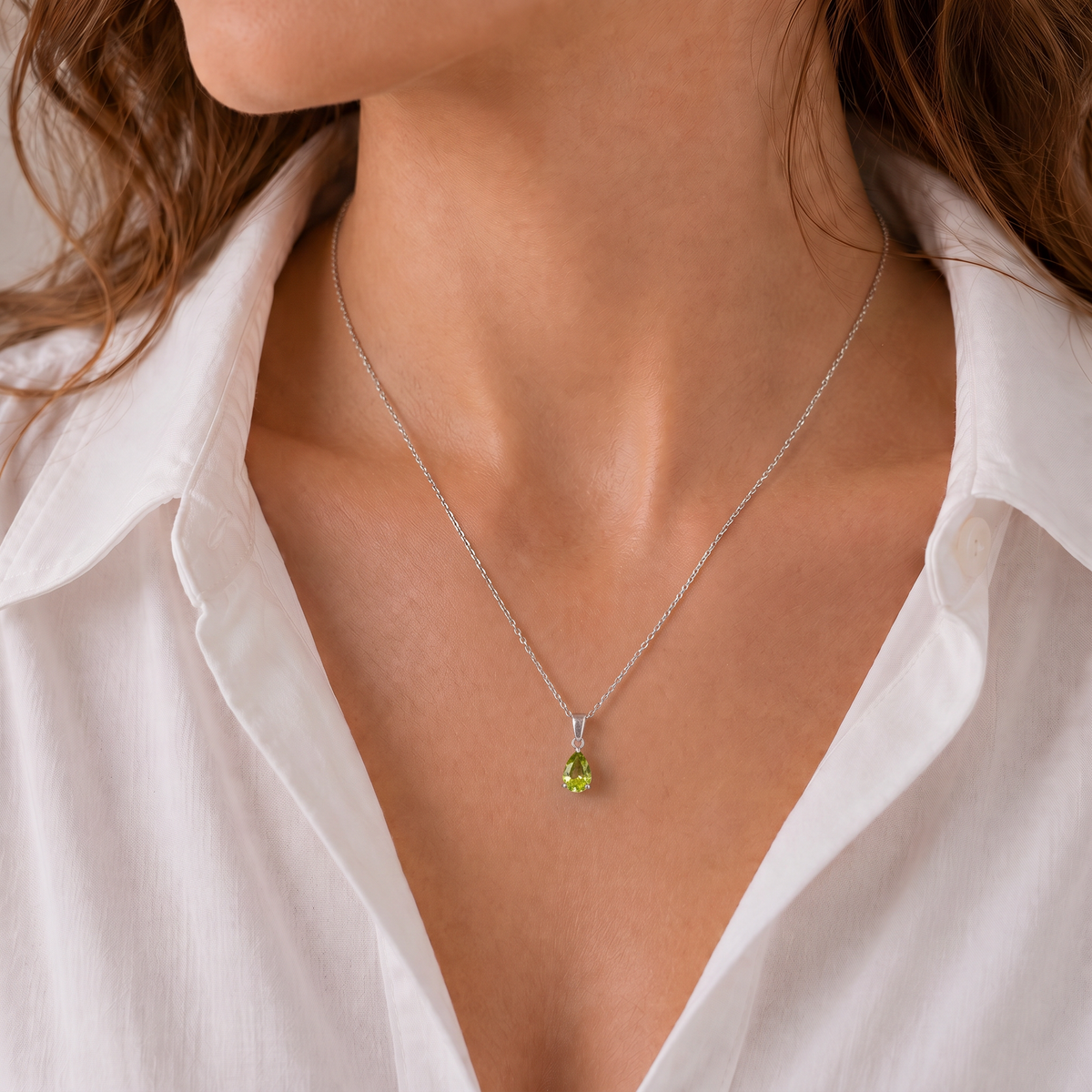 woman Model wearing a natural peridot teardrop necklace in sterling silver with an open-collar white shirt.