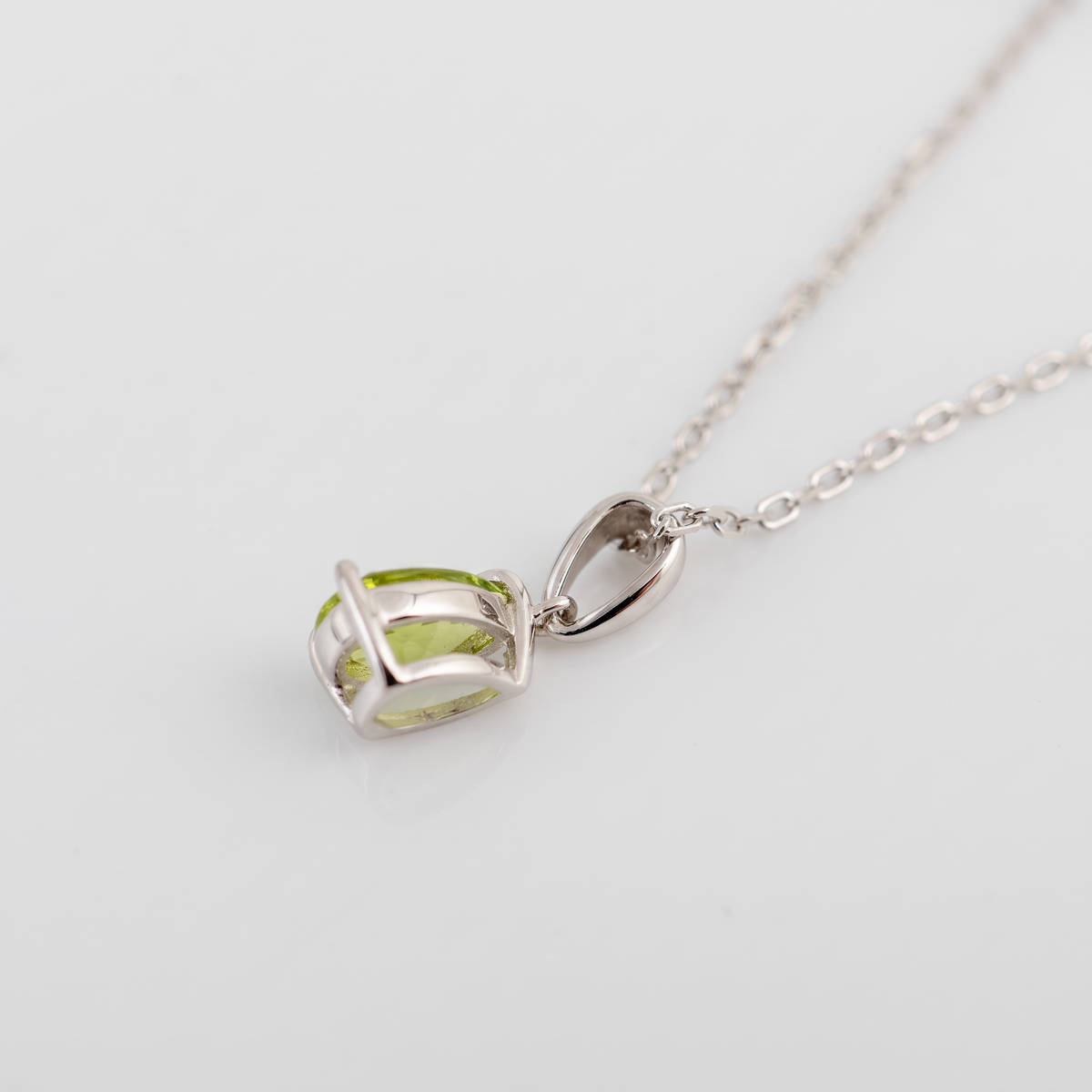 Side view of a natural peridot teardrop necklace in sterling silver, showing the open gemstone setting, claws and tapered bail on a white surface.