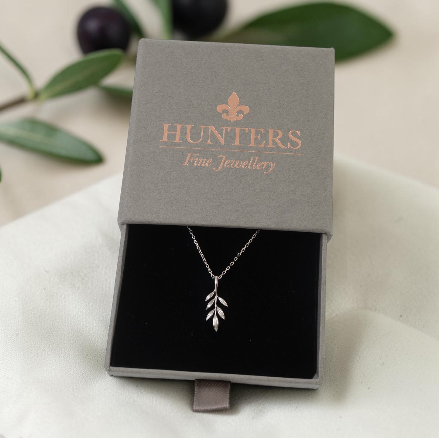 Silver olive branch necklace in a 'Hunters Fine Jewellery' box with leaves in the background