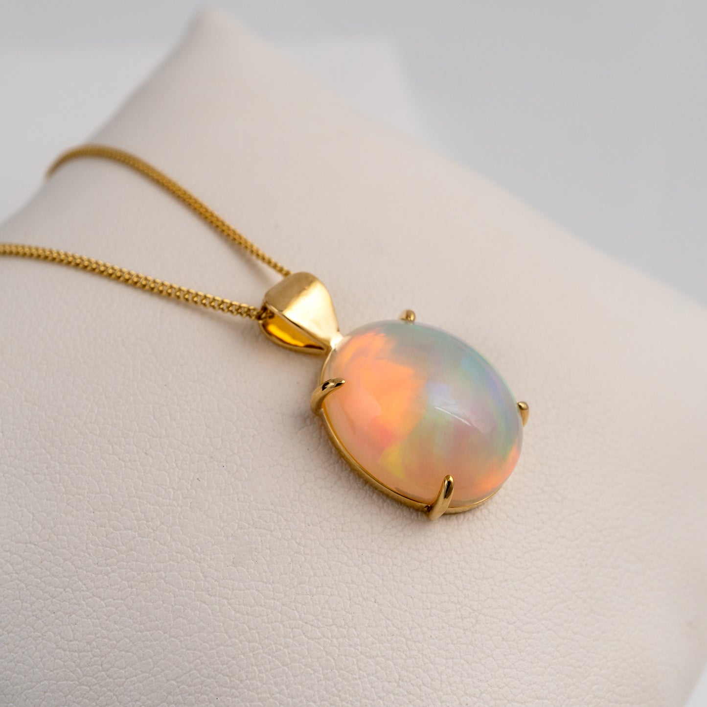 Opal pendant on a gold chain against a neutral background