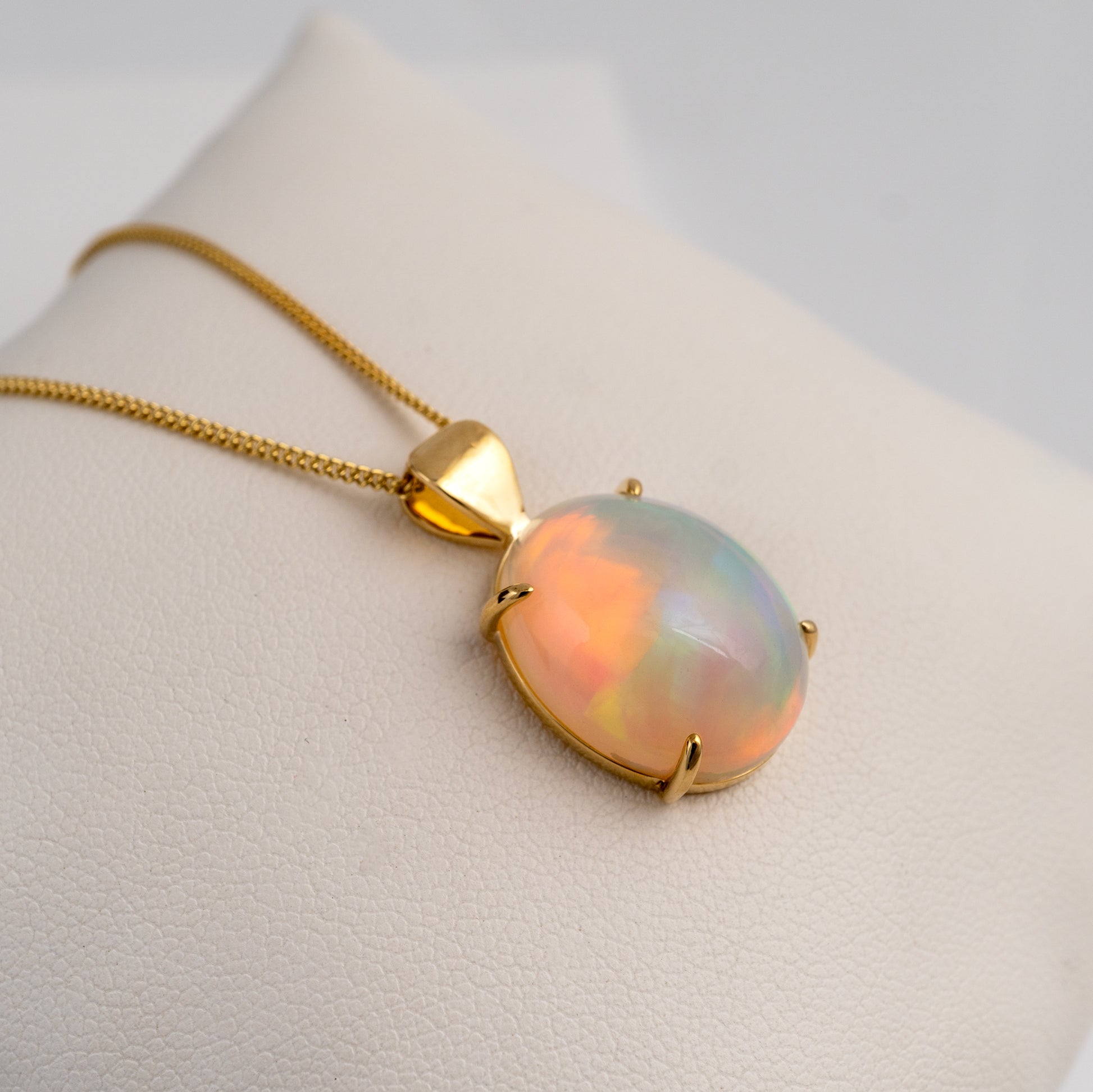 Opal pendant on a gold chain against a neutral background