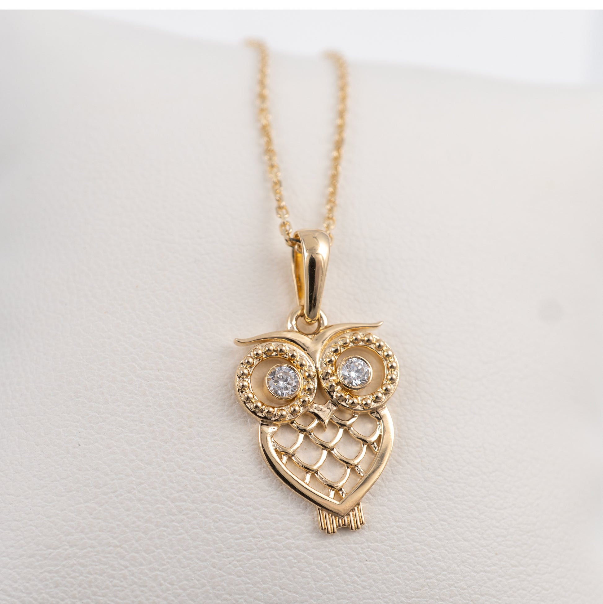 Gold owl-shaped pendant necklace on a light gray background