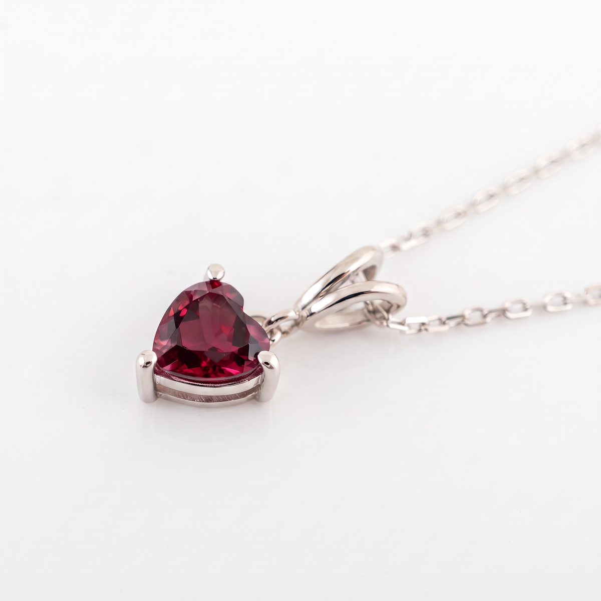 lab ruby heart necklace silver setting close up view laid on smooth white surface