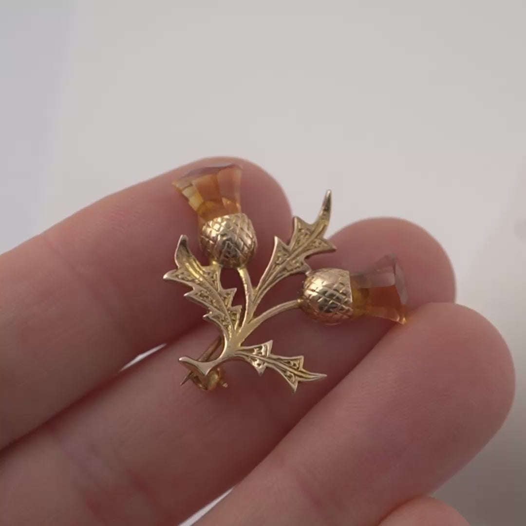 Product video of a gold Scottish thistle brooch with citrine gemstones, showing scale and intricate details while being turned by hand