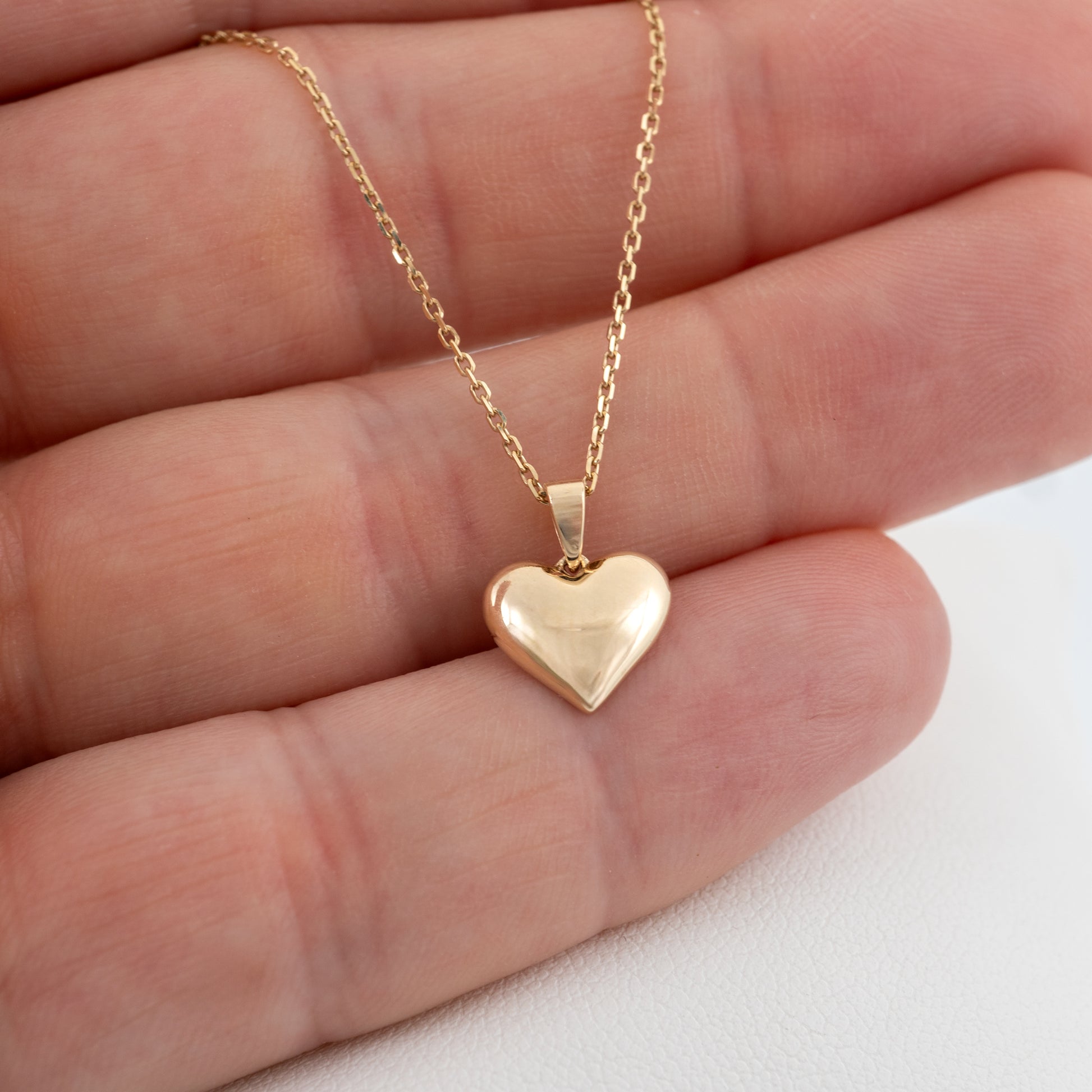 Small gold heart pendant necklace shown in hand for scale