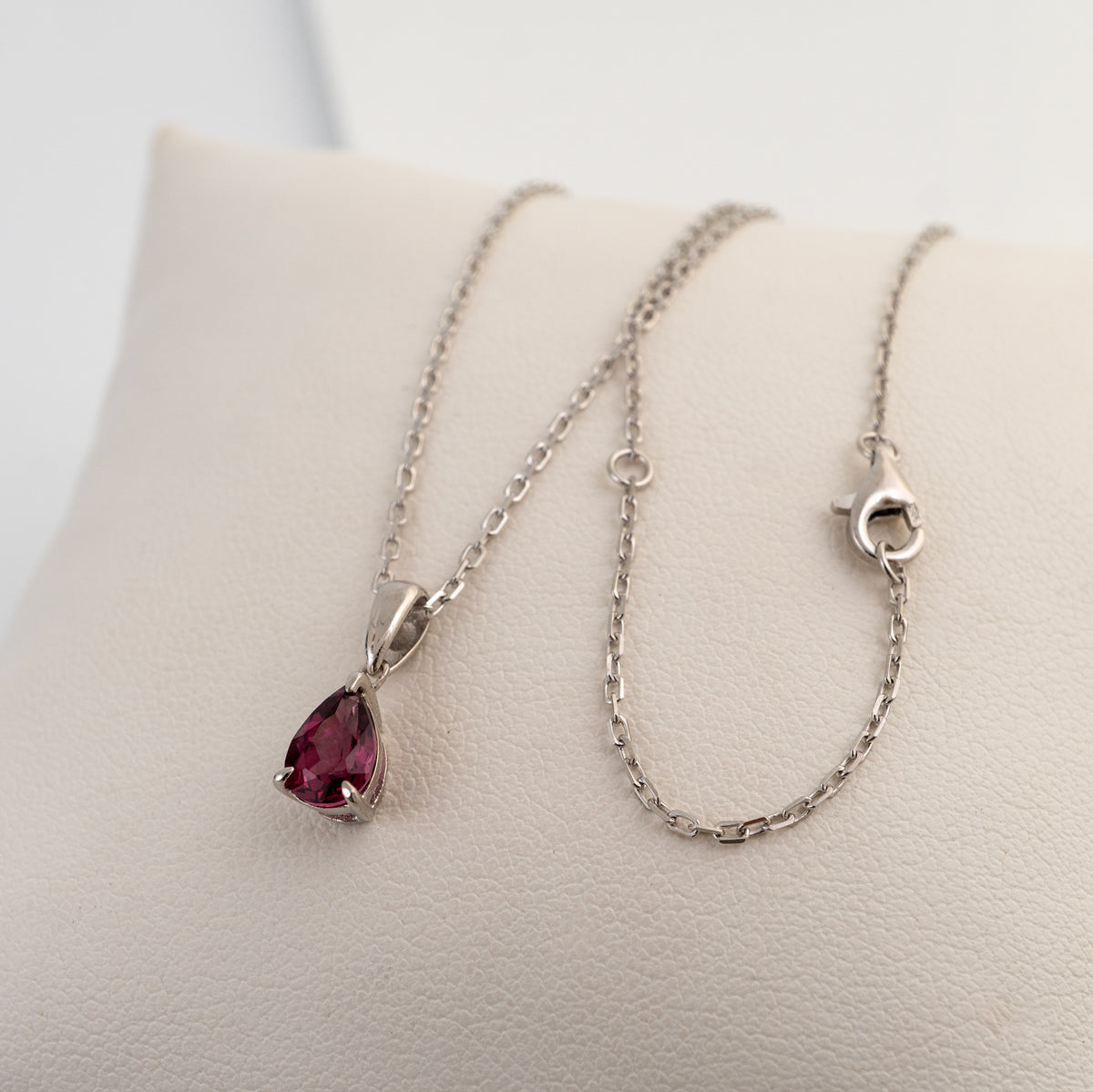 Rhodolite garnet teardrop necklace showing the sterling silver chain, adjustment ring and lobster clasp on a white cushion.