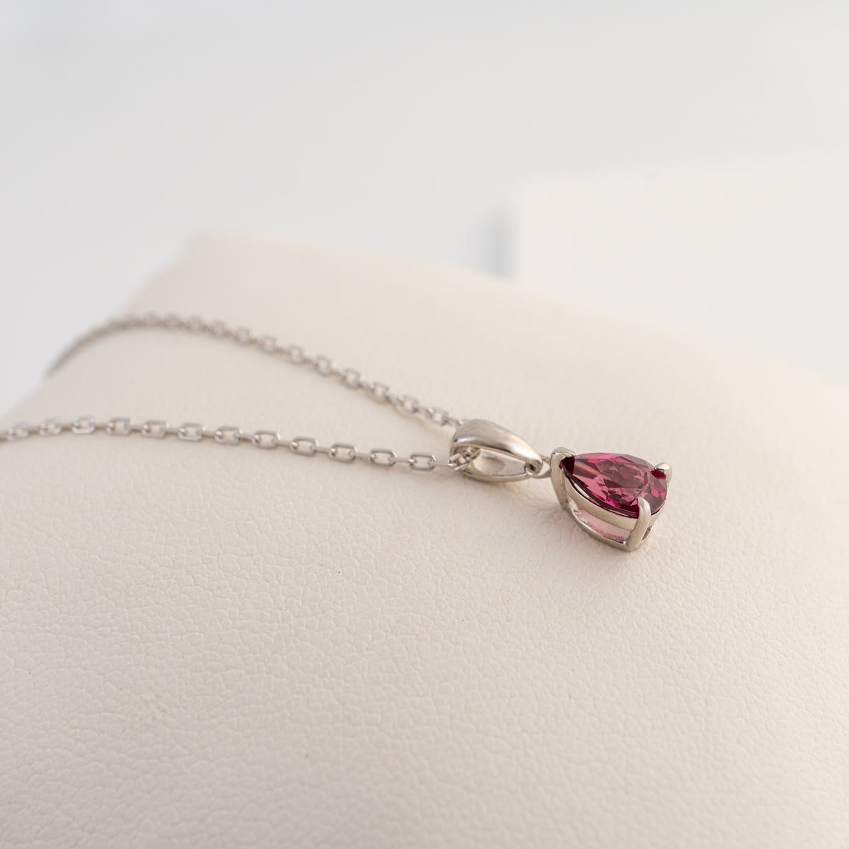 Angled view of the pink pear-cut rhodolite garnet pendant showing its sterling silver claw setting and polished bail.