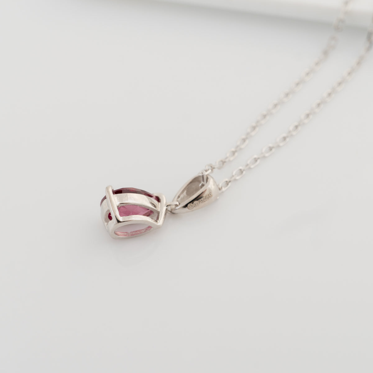 Side view of the rhodolite garnet pendant showing its open sterling silver setting, tapered bail and chain.