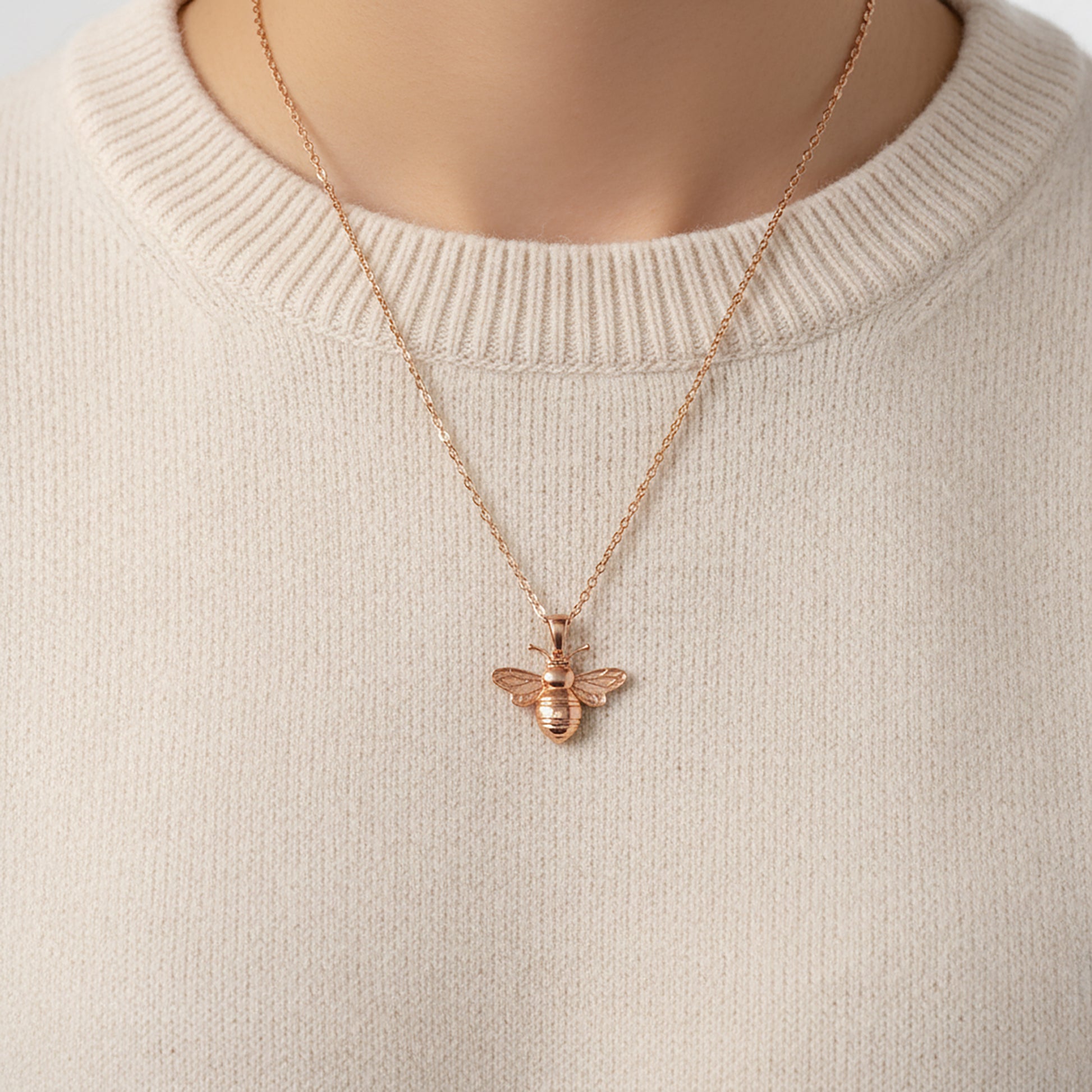 Rose gold bee necklace worn by a model with a beige sweater