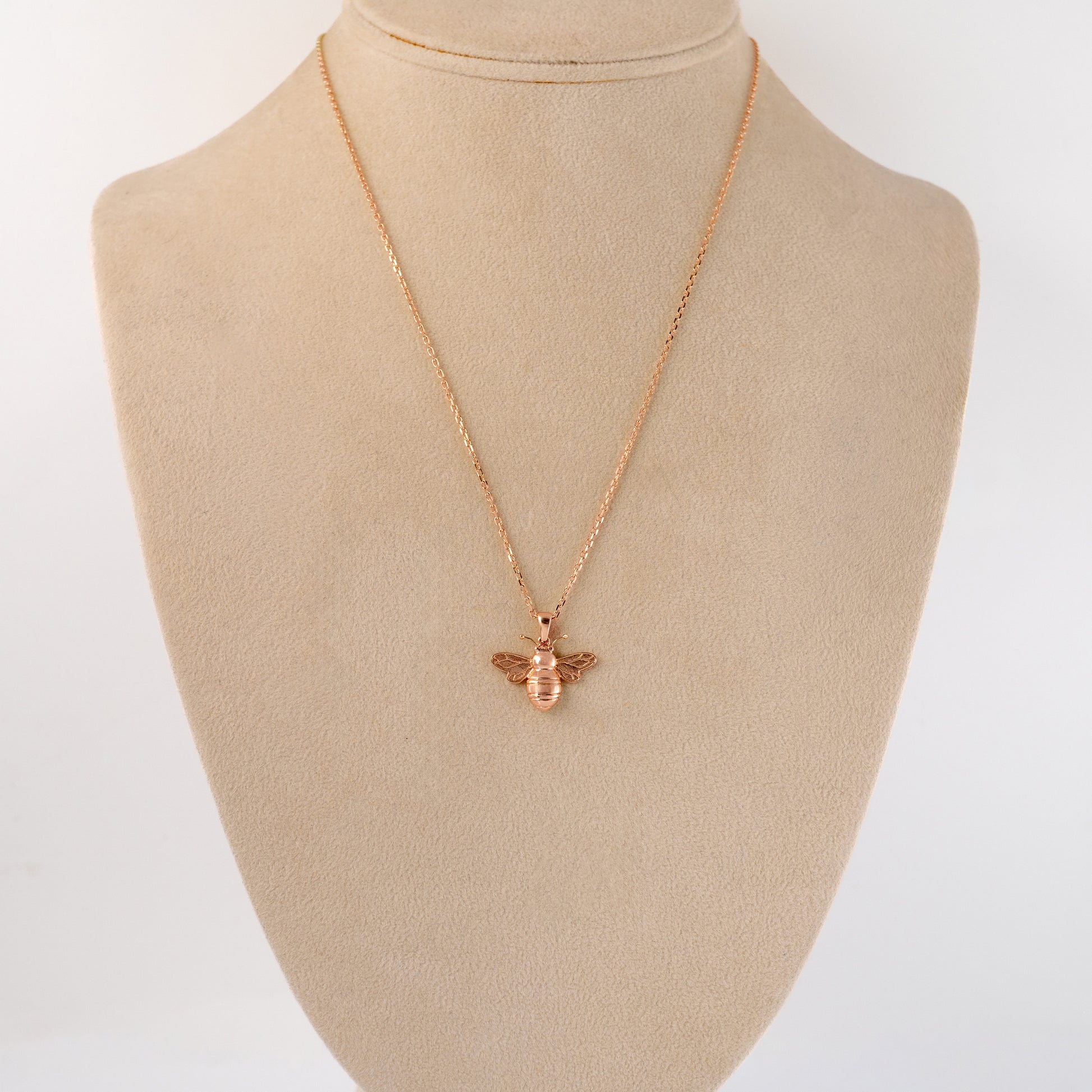 Rose gold bee necklace on a beige mannequin bust with a white background