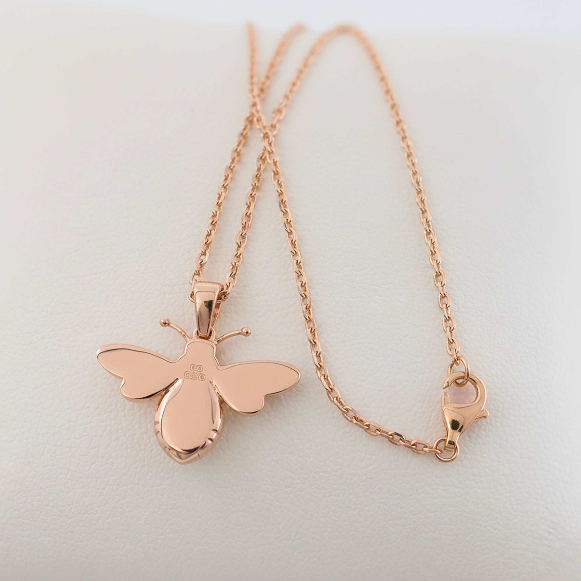 Rose gold bee pendant necklace smooth back with hallmarks and chain with lobster clasp plain light grey background 