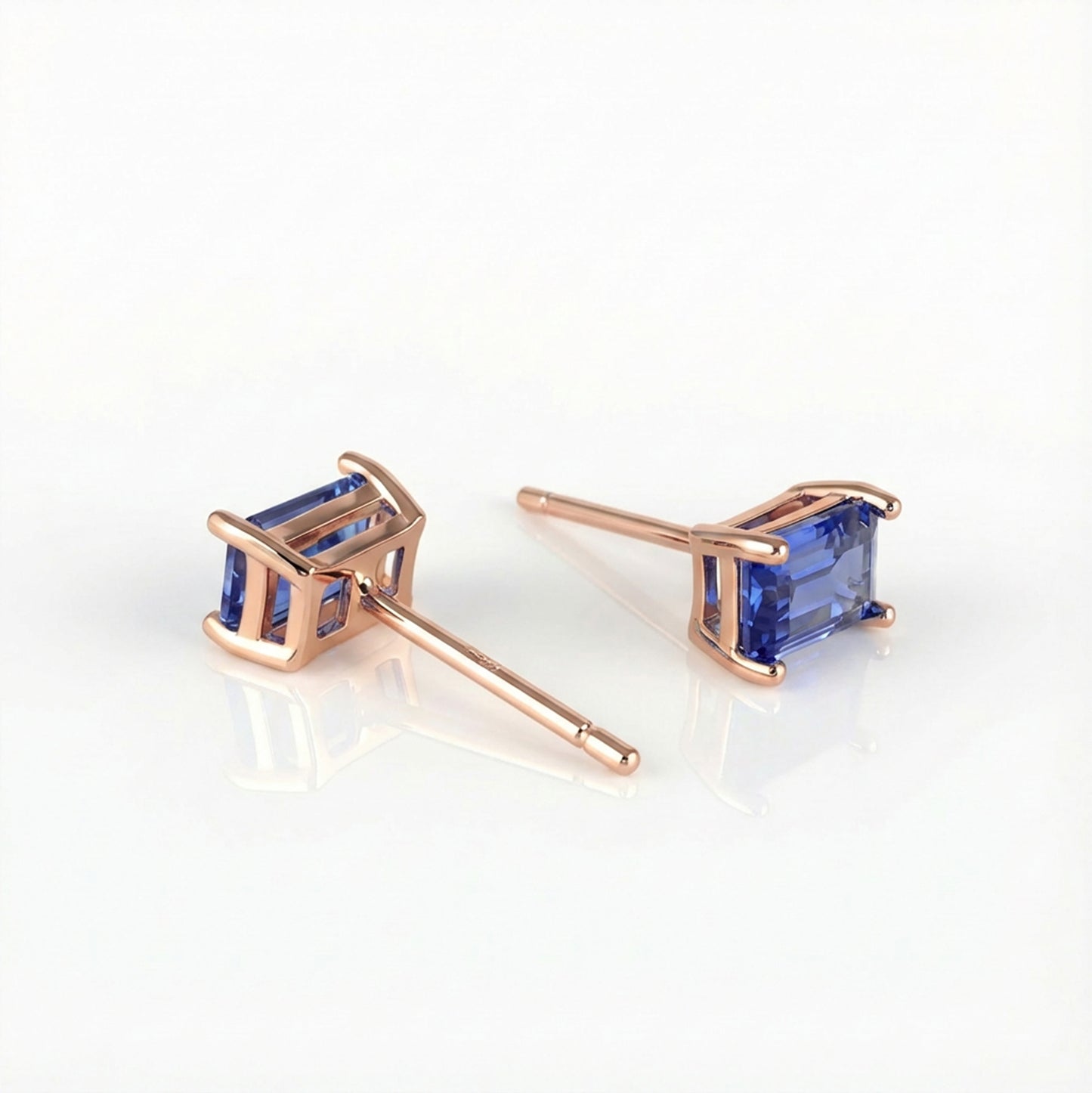Rose gold earrings with lab sapphire blue gemstones on a white background