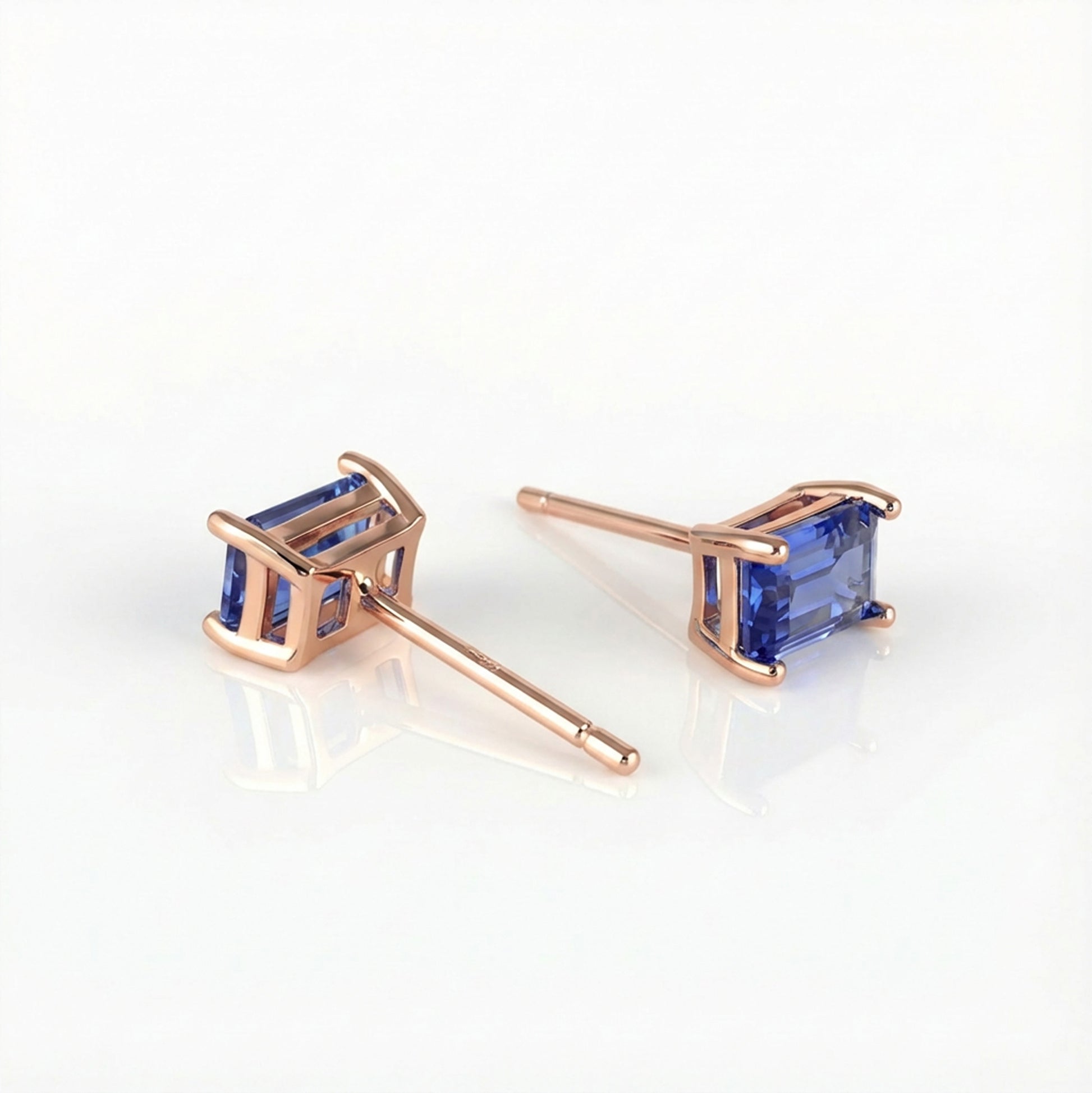 Rose gold earrings with lab sapphire blue gemstones on a white background