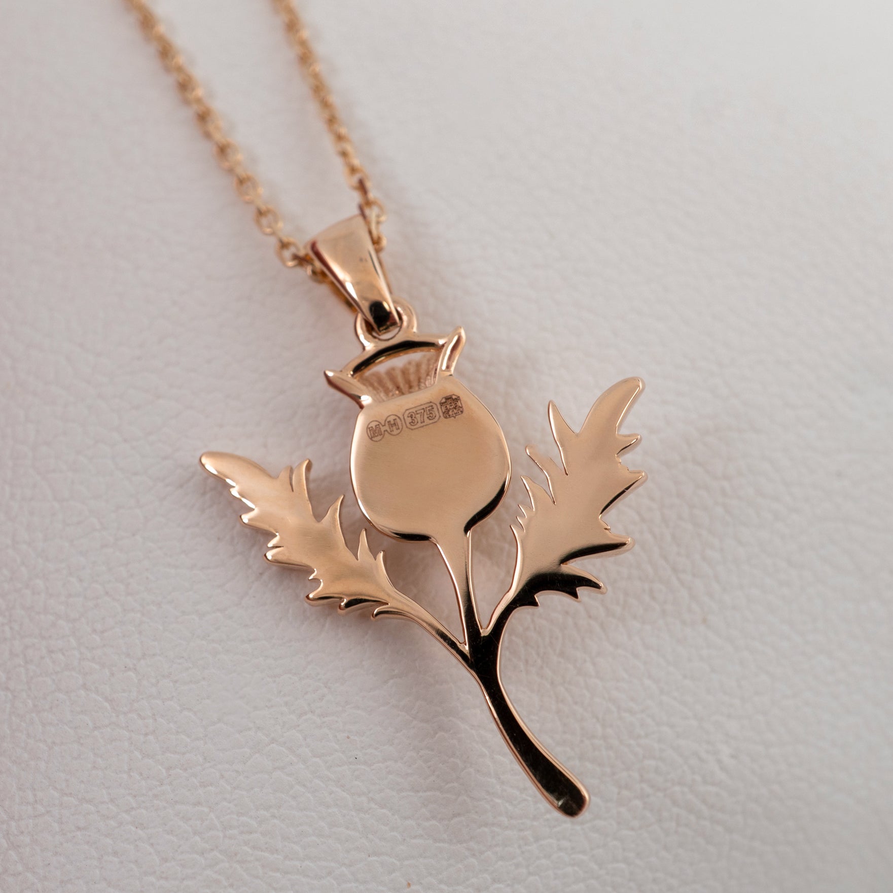 Rose gold thistle pendant necklace smooth back with edinburgh assay hallmarks on a light gray background