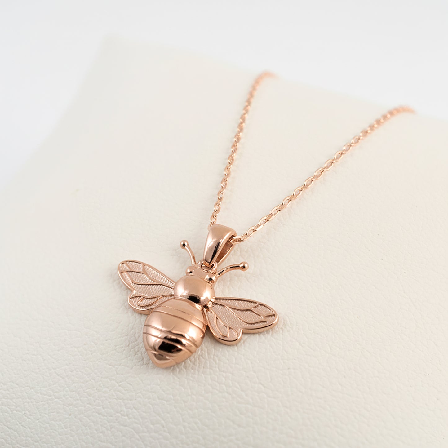 Rose gold bee pendant necklace on a light background