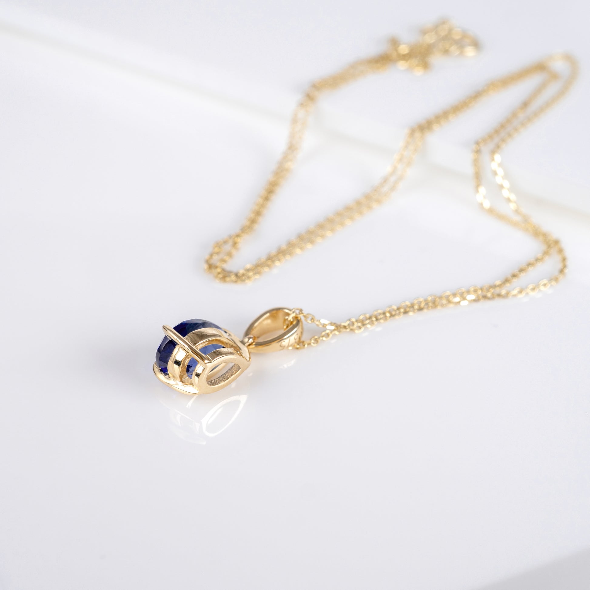 A gold chain necklace with a small pendant featuring dark blue inlaid details, displayed on a clean white surface.