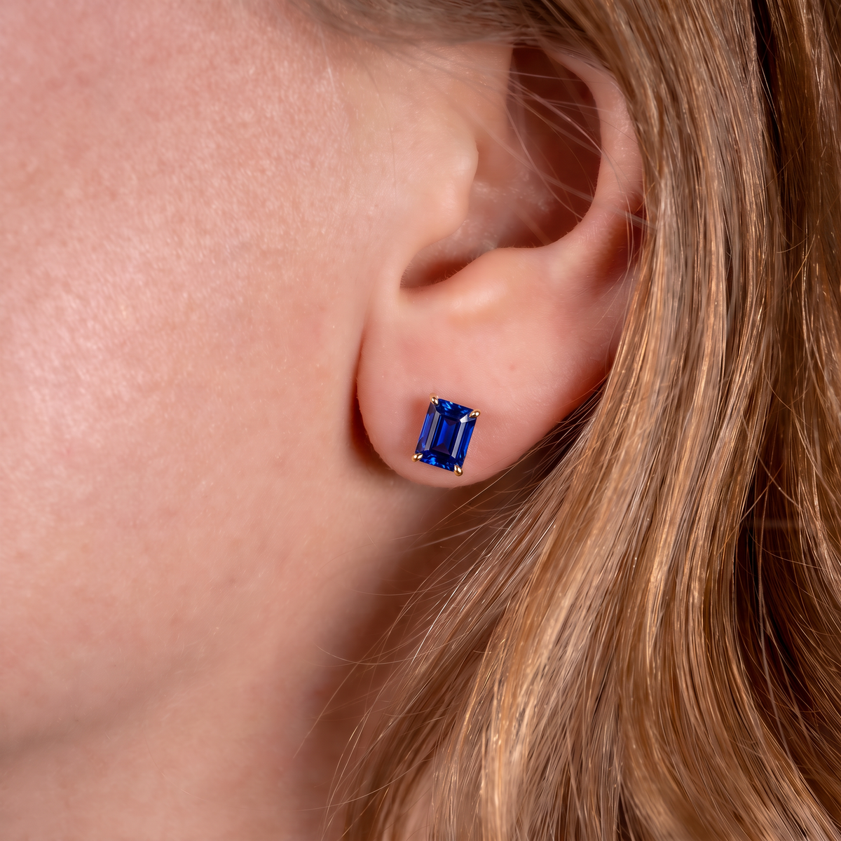 Royal blue rectangle sapphire stud earring worn on the ear