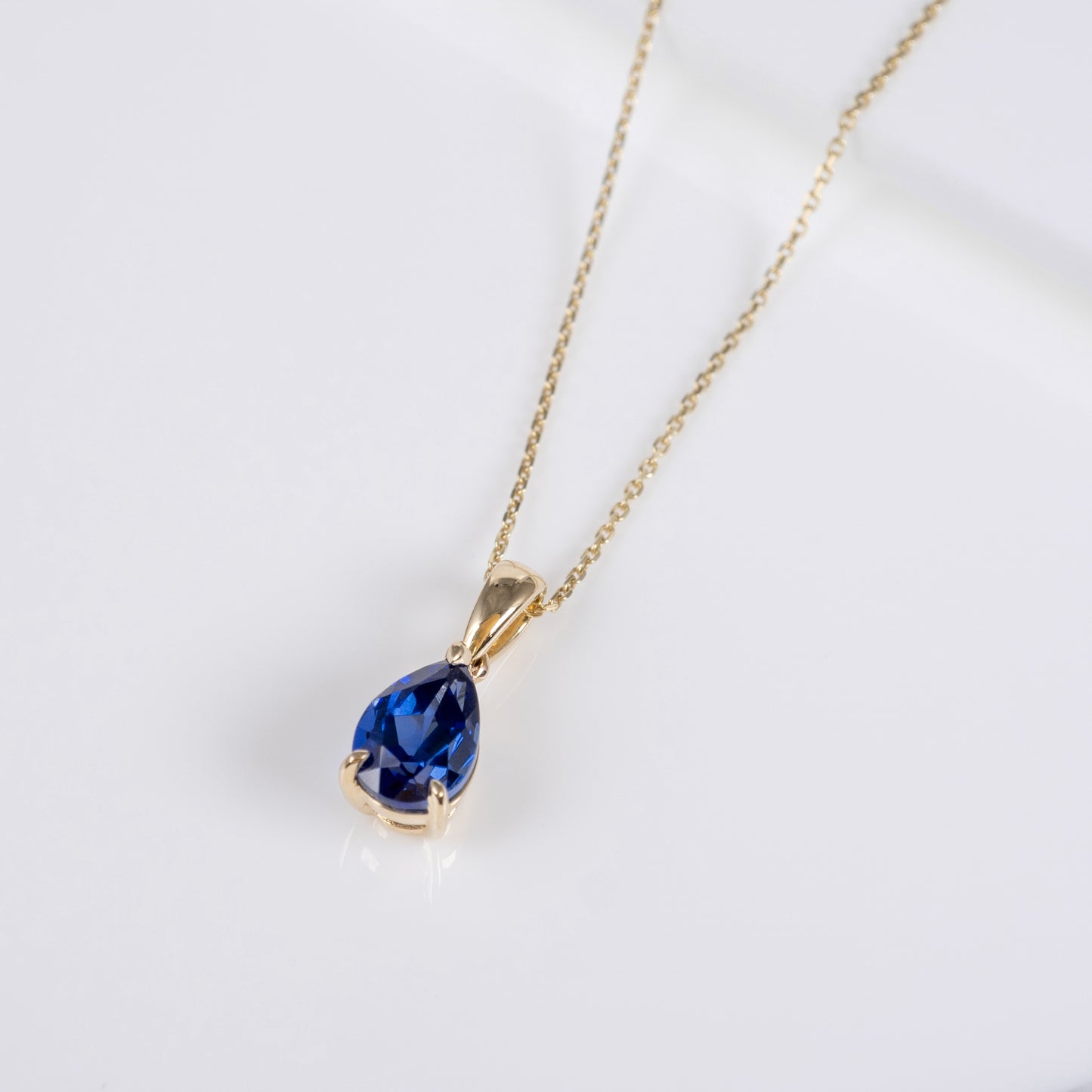 A gold chain necklace with a teardrop-shaped deep blue gemstone pendant, displayed on a clean white background.