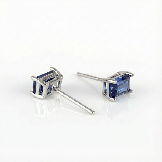 A pair of silver stud earrings with rectangular blue gemstones, displayed on a clean white reflective surface.