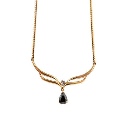 A gold necklace with a twisted chain, a curved wing-like pendant, a small clear accent stone, and a teardrop-shaped dark  blue gemstone at the center, shown on a plain white background.