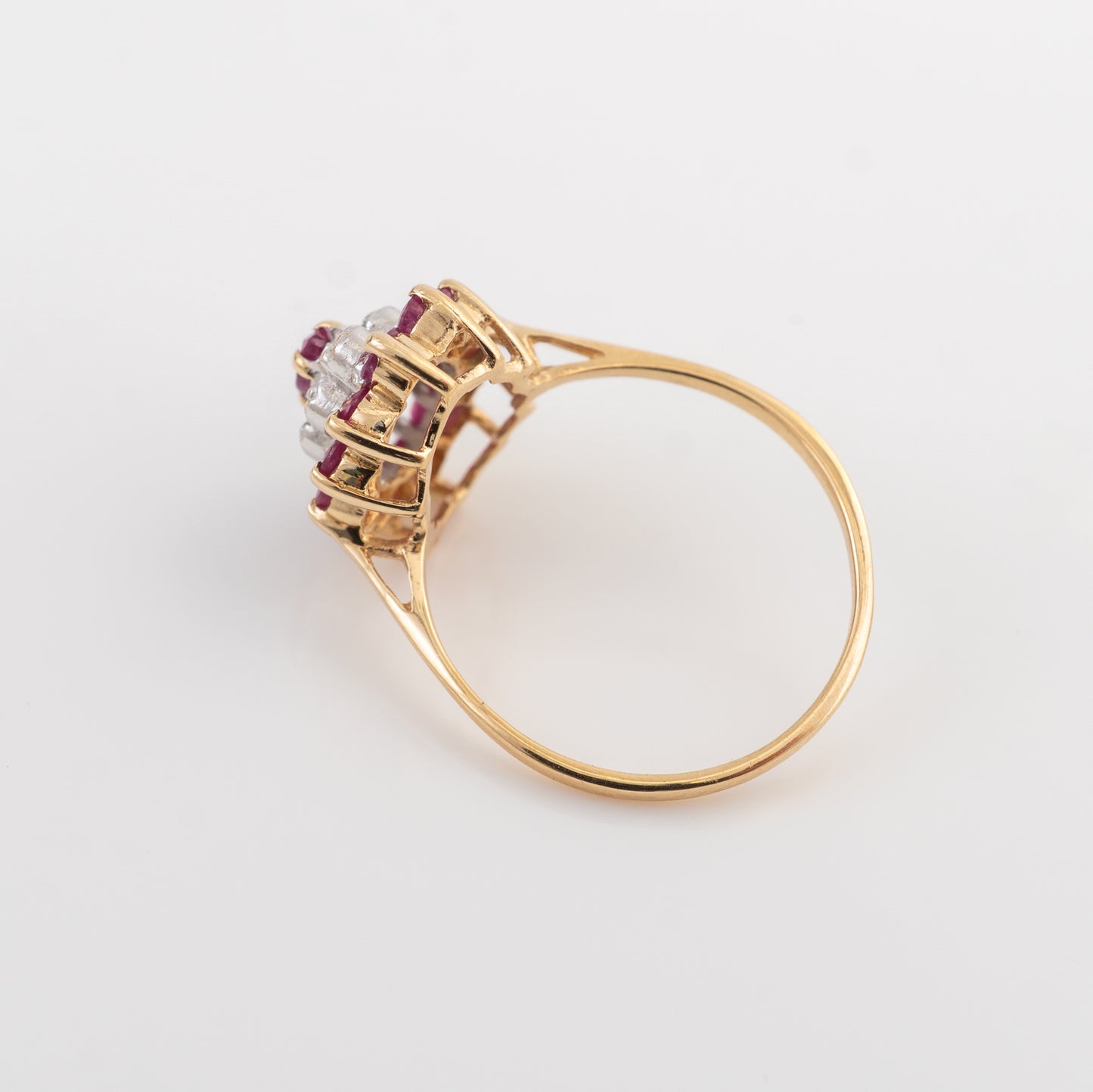 A yellow gold ring featuring a cluster setting with clear round-cut stones and small pinkish-red accent stones, shown on a plain light gray background.