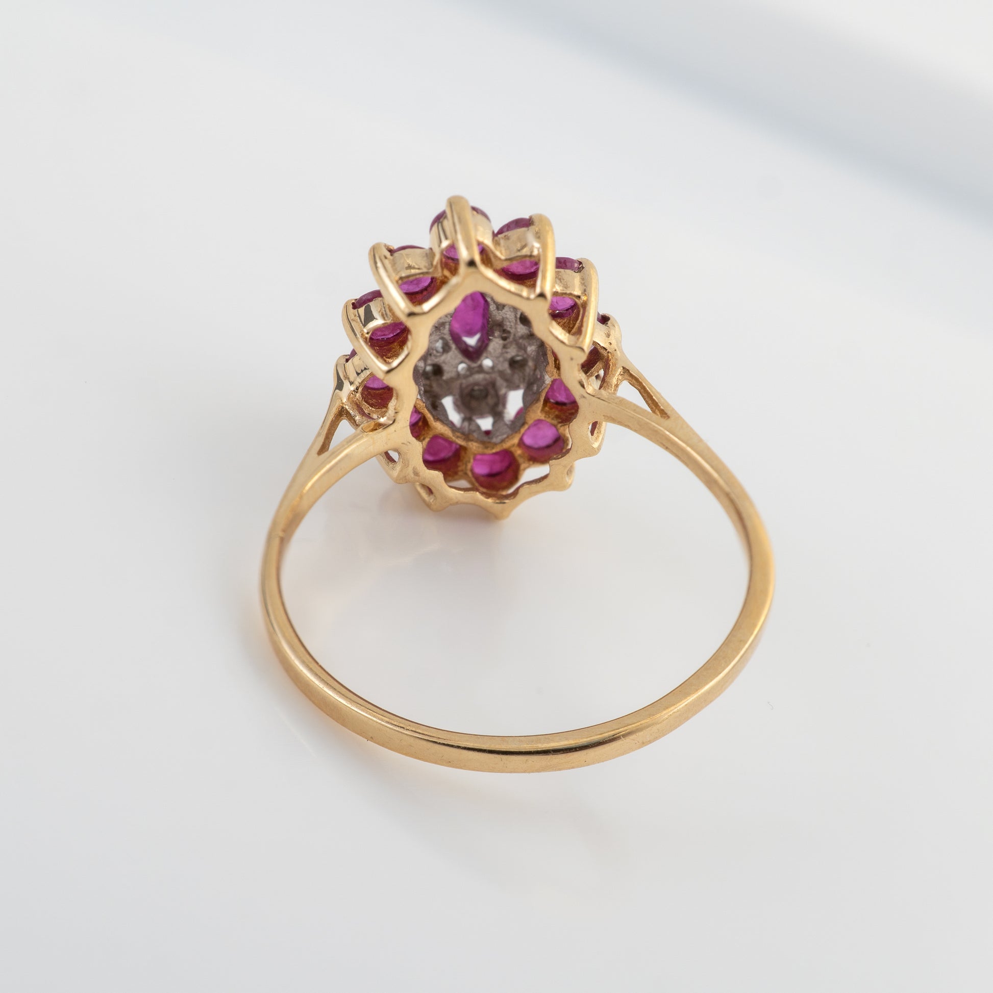 A gold ring featuring a central pear-cut gray gemstone surrounded by a cluster of small round pink gemstones and tiny clear stones, set on a plain light gray background.