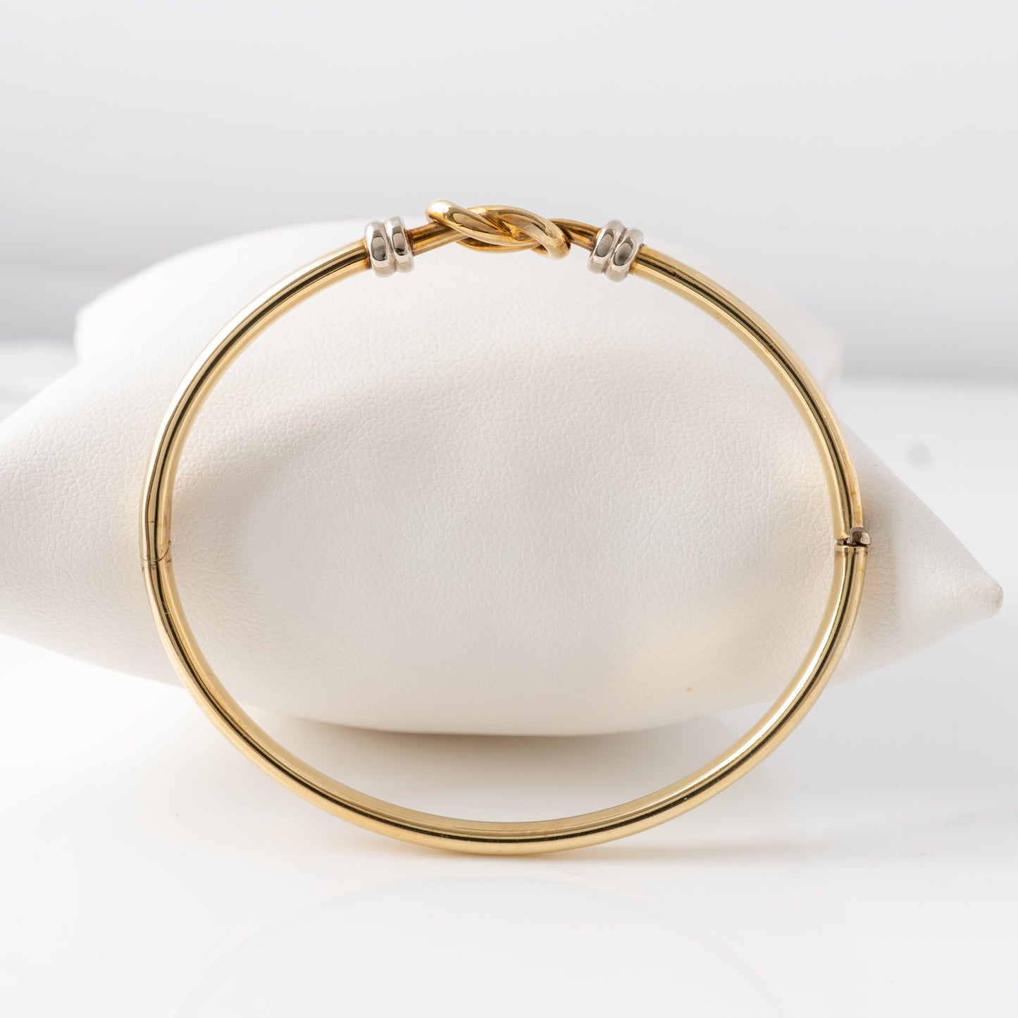 A side profile view of the 9ct gold loop knot bangle with white gold accents, displayed on a cushion