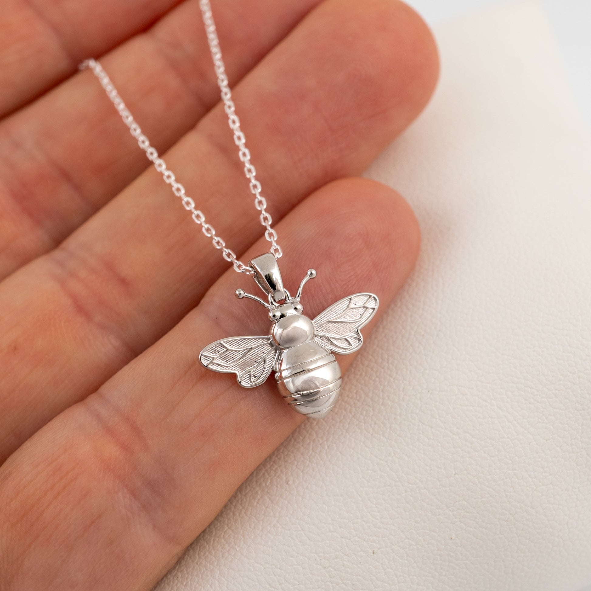 Silver bee pendant necklace held in a hand against a light background