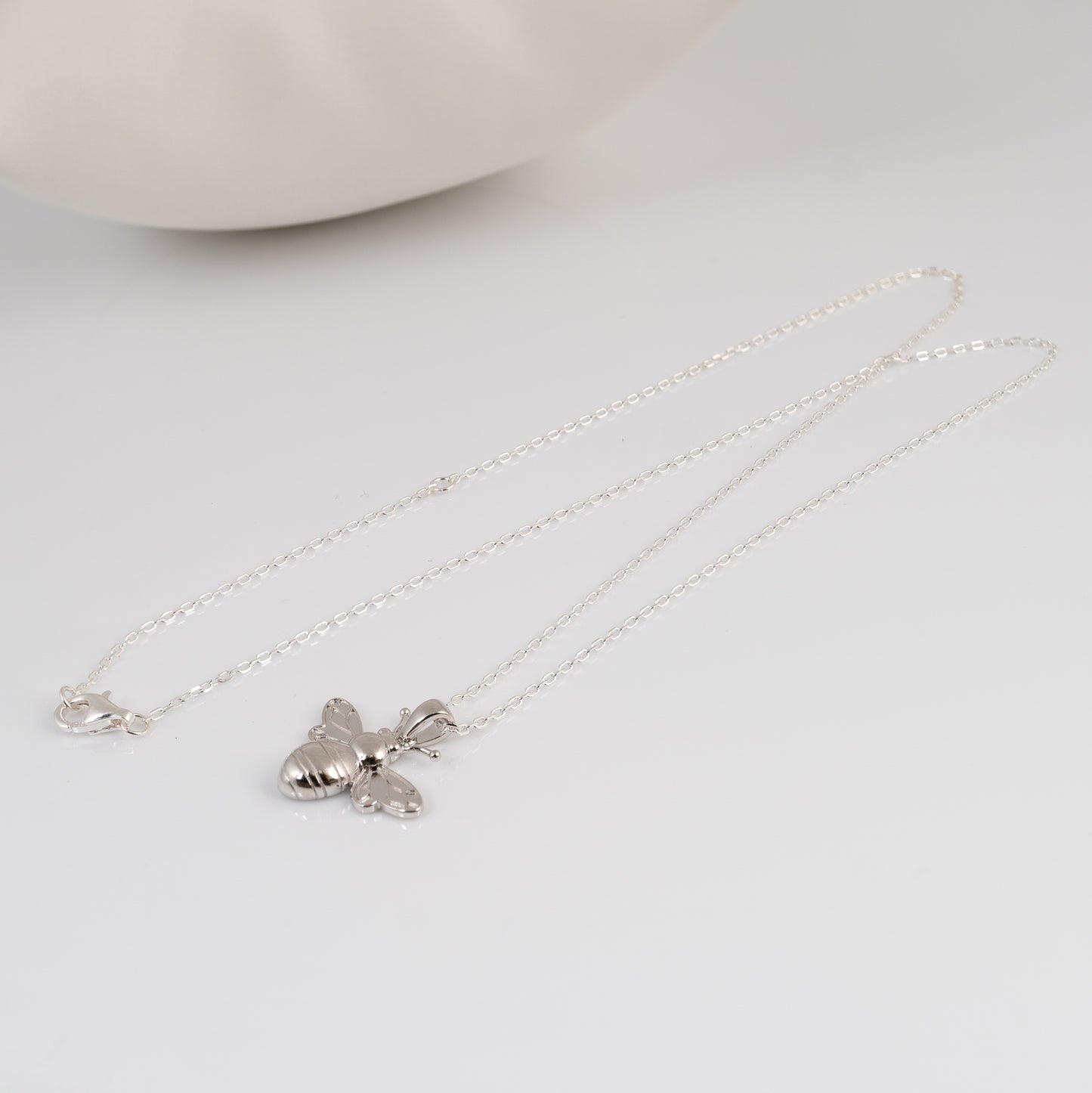 Silver necklace with a bee pendant on a light gray background