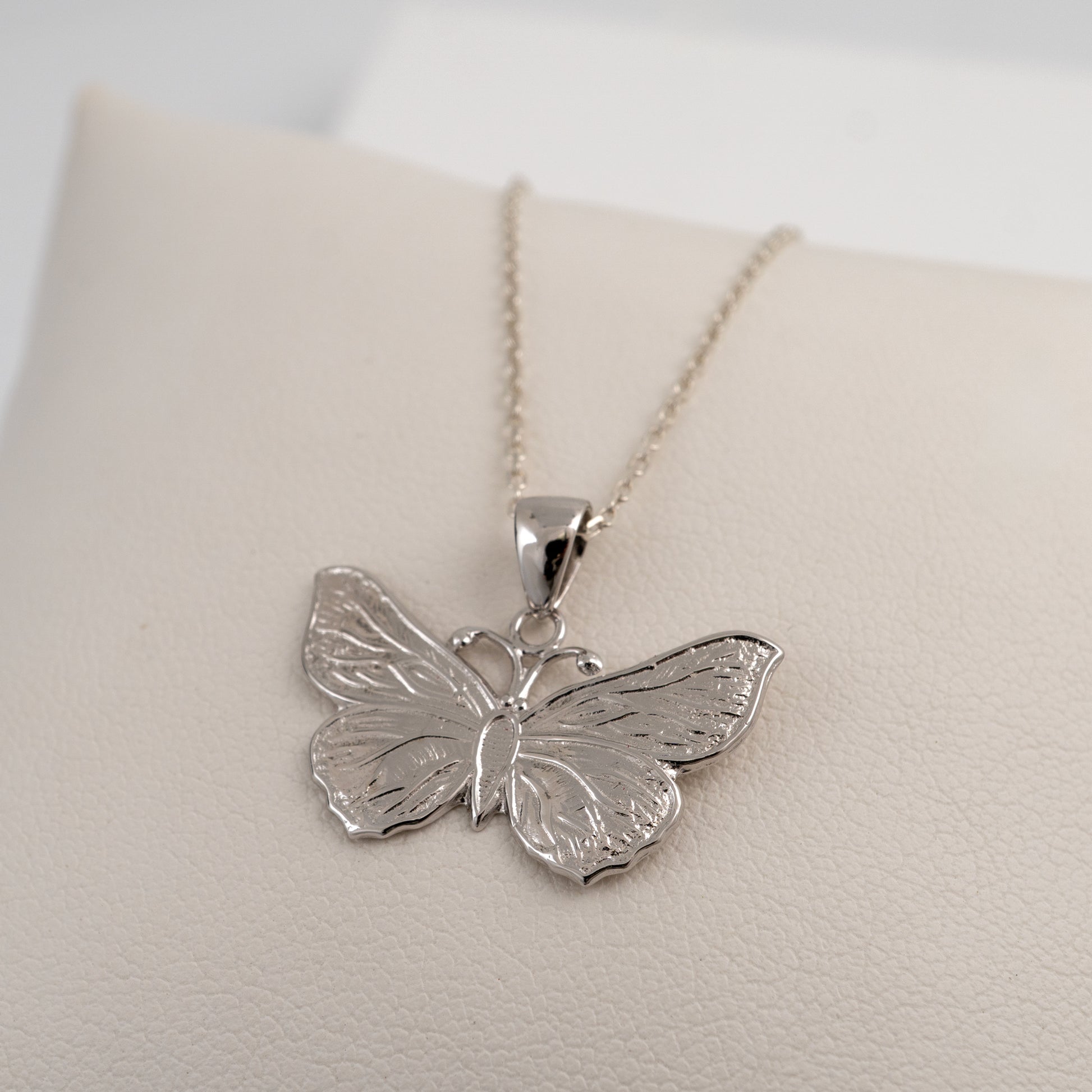 Silver butterfly pendant on a chain against a light background