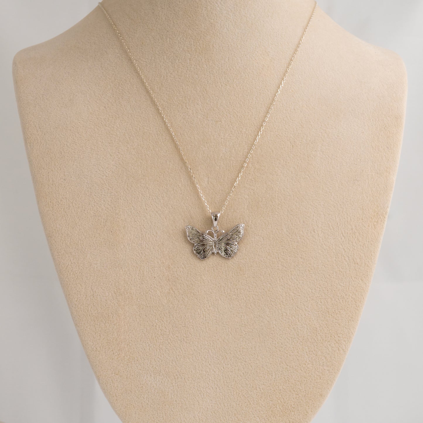 Butterfly pendant necklace on a beige mannequin bust with a plain background